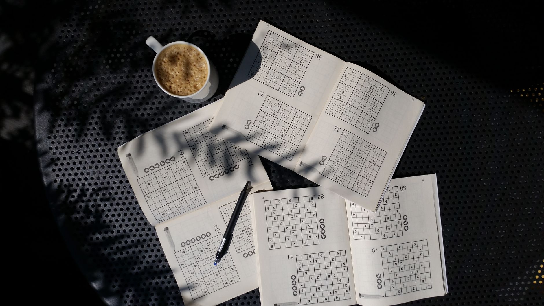 carnets de sudoku ouverts sur une table avec un stylo et une tasse de café