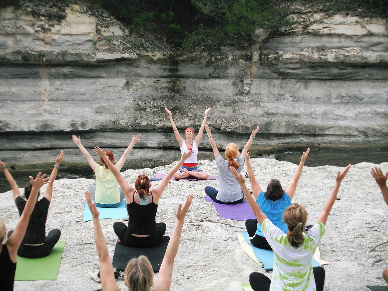 Groupe de femmes en cours de yoga en plein air sur des tapis, bras levés, face à une animatrice, au pied d'une falaise calcaire